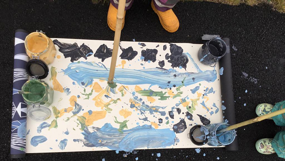 Barnen målar med stora penslar ute.